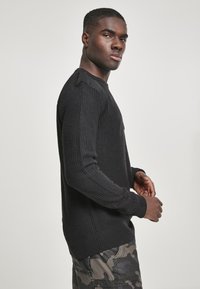Suéter negro de punto acanalado con mangas largas y acentos en los hombros, combinado con pantalones cargo de camuflaje. Diseño estructurado y texturizado.