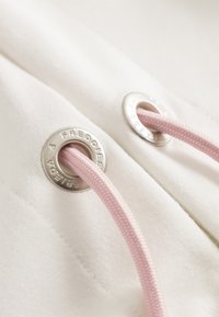 Witte stof met zilveren metalen oogjes en een lichtroze trekkoord. Close-up toont de stiksels en textuurdetails.
