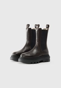 Stivali Chelsea in pelle marrone con pannelli elastici laterali, suola in gomma dentellata e tessuti per il sollevamento. Texture liscia con dettagli di cucitura minimi.