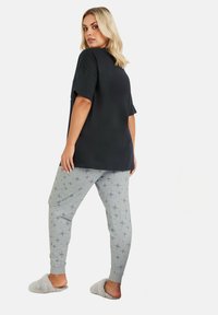 Camiseta negra de gran tamaño, pantalones de pijama grises con un patrón, y zapatillas de casa grises y esponjosas. Los pantalones tienen un patrón de explosión de estrellas en azul.