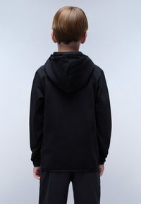 Zwarte hoodie met een capuchon en lange mouwen, gemaakt van een gladde, dikke stof. Opvallende naden bij de taille en mouwen, gedragen met zwarte broek.
