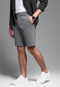 Graue Shorts aus weichem Material, taillierte Passform, seitliche Taschen, kombiniert mit weißen Turnschuhen und einem schwarzen T-Shirt, was einen lässigen Stil unterstreicht.