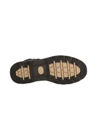 Gummisula på en sko med en strukturerad svart yta och beige detaljer, som har ett rutmönster för grepp och stabilitet.