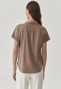 Lyhythihaisen ruskean paidan kaulusta, jossa on laskettu takaosa ja kaareva helma. Silkkinen kankaan pinta.