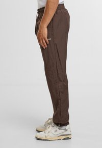 Brązowe lekkie spodnie z tkaniny z elastycznym pasem, bocznymi kieszeniami i mankietami, zestawione z off-white sneakersami.