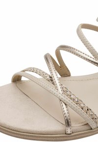 Strappy sandal with a beige faux suede sole, metallic gold and patterned straps, featuring a textured finish and a cushioned footbed.