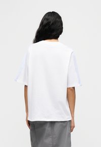 Λευκό φαρδύ t-shirt με κοντά raglan μανίκια, με ανοιχτό μπλε λεπτομέρειες στους ώμους και απαλή βαμβακερή υφή.