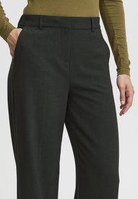 Tmavohnedé formálne nohavice s hladkým povrchom, pútkoch na opasok a bočnými vreckami. Majú rovný strih, ktorý zaisťuje elegantný vzhľad.
