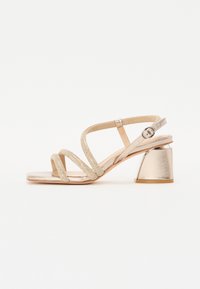 Sandale dorée à brides avec un dessus texturé, bout carré et un talon bloc métallique et anguleux. Comprend une bride ajustable au niveau de la cheville.