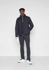 Tamsi dygsniuota striukė su aukštu apykakliu, derinama su ilgarankoviu viršutiniu rūbu ir tamsiomis kelnėmis. Komplektą papildo pirštinės ir golfo batai.