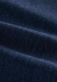 Granatowa tkanina dżinsowa o miękkiej strukturze i subtelnych pionowych paskach, ukazująca lekko błyszczące wykończenie oświetlone naturalnym światłem.