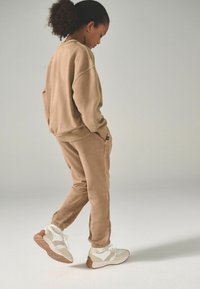 Tröja i tan och matchande joggingbyxor i mjukt tyg, med elastiska mudd. Vita och beige sneakers fulländar outfiten med gummisula.