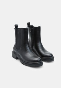 Melna ādas potītes zābakus ar elastīgām sānu daļām, aizmugurējo cilpu un priekšējo rāvējslēdzēju. Biezs, teksturēts gumijas zole, kas nodrošina saķeri.