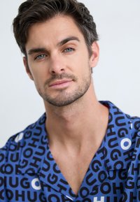 Short-sleeve shirt featuring a blue background with black and white text patterns, button-down collar, and soft fabric texture.