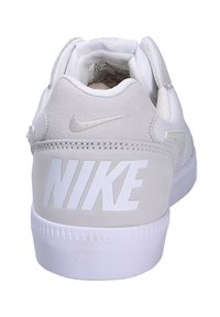 Zapatillas Nike blancas con materiales de ante y malla, que presentan un gran logo blanco en el talón y una suela de goma texturizada.