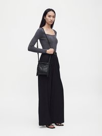 Femme portant un haut côtelé gris ajusté, un pantalon noir taille haute à jambes larges, des sandales noires et un sac bandoulière en cuir noir avec des franges.