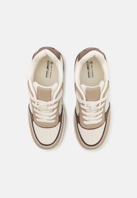 Baskets véganes marron et crème avec détails perforés, bout rond et lacets plats. Accents texturés et logo sur la doublure intérieure.