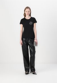 T-shirt nera in cotone con scollatura rotonda e maniche corte, caratterizzata da un design grafico argentato sul petto. Abbinato a pantaloni in pelle sintetica nera.