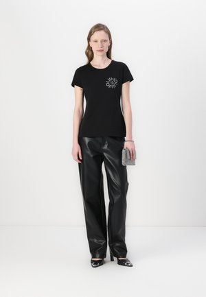 T-shirt nera in cotone con scollatura rotonda e maniche corte, caratterizzata da un design grafico argentato sul petto. Abbinato a pantaloni in pelle sintetica nera.