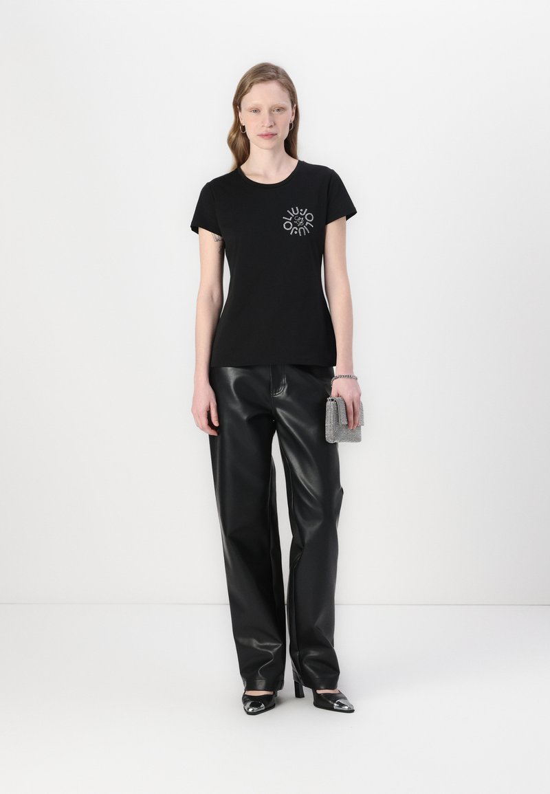 T-shirt nera in cotone con scollatura rotonda e maniche corte, caratterizzata da un design grafico argentato sul petto. Abbinato a pantaloni in pelle sintetica nera.