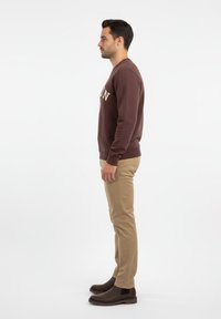 Sudadera marrón con cuello redondo, pantalones beiges y botas de tobillo marrones oscuras. Tejido suave, texto bordado en la parte delantera, ajuste casual.