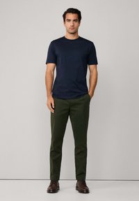 En marineblå t-skjorte med korte ermer kombinert med mørkegrønne chinos og brune snøredesignede sko. Stoffet ser jevnt ut med en avslappet passform.