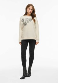 Ljusgrå sweatshirt med svart blommönster, rund hals, nedsläppta axlar; parat med smala svarta jeans och ankelboots.