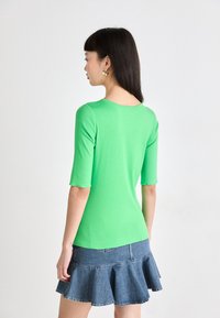 Haut vert ajusté avec des manches trois-quarts, associé à une jupe en denim évasée. Texture lisse, design simple et couleur vive.