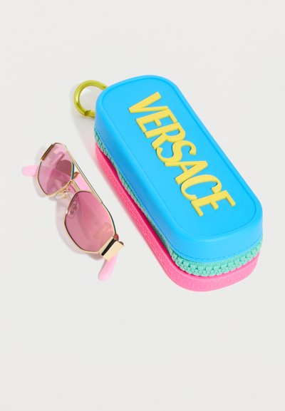 Μπλε, ροζ και πράσινη θήκη γυαλιών ηλίου Versace με κίτρινο λογότυπο δίπλα σε γυαλιά ηλίου με χρυσό πλαίσιο που έχουν ροζ φακούς και ροζ άκρα στα ναούς.