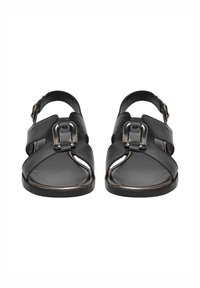 Černé kožené sandály se zapínáním na přezku, otevřenou špičkou, překříženými pásky a plochou podrážkou. Hladký povrch s kovovými ozdobami.