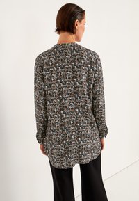 Langarmshirt mit einem dunklen Blumendruck in Brauntönen, Blau und Weiß. Asymmetrischer Saum und weiche Stofftextur.