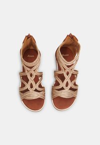 Ruske sandale s križanjem trakama u metalik zlatnoj boji, sa niskim potpeticom i zatvaranjem na zipu straga. Glatka kožna uložak.