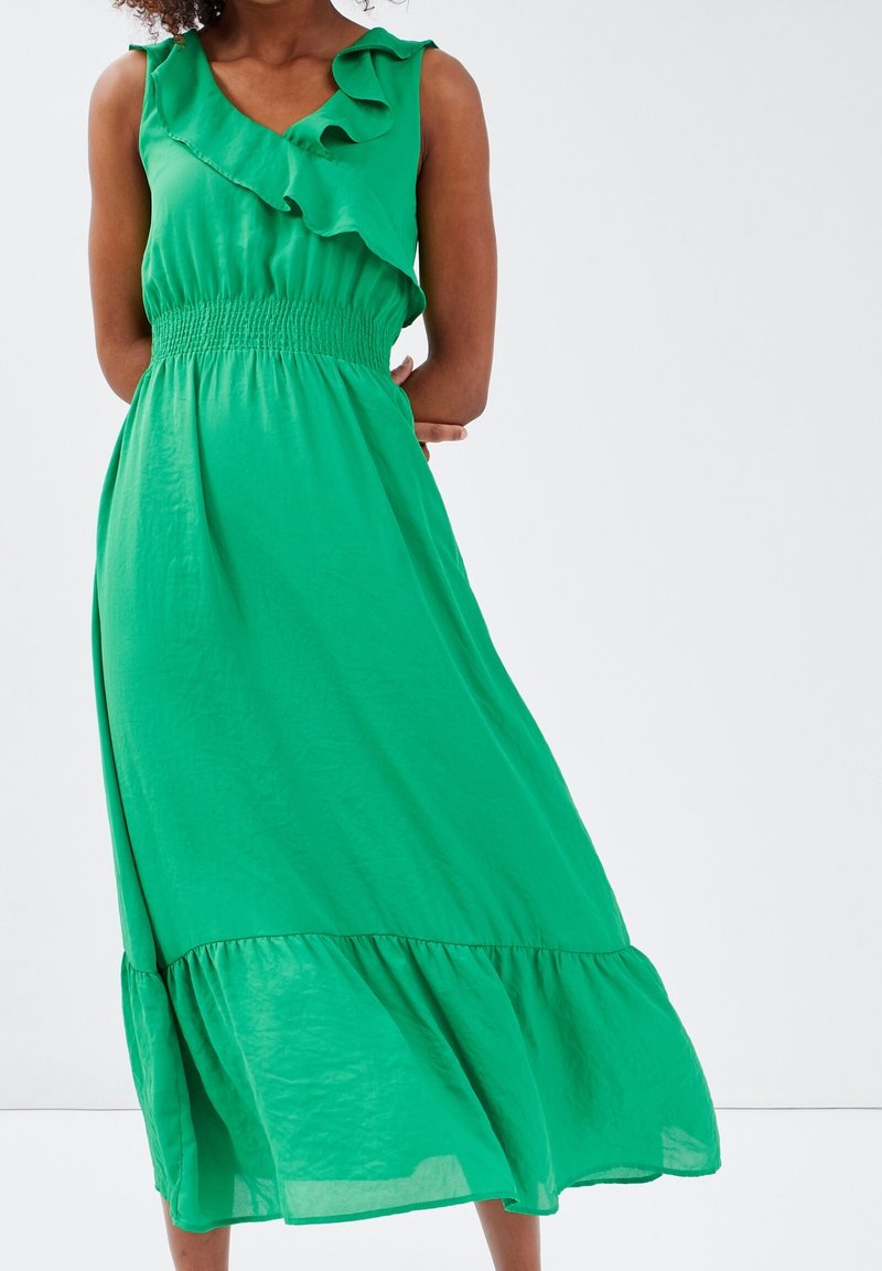 Robe maxi verte avec une taille smockée, un décolleté à volants, et une jupe fluide. Fabriquée en tissu léger, avec un ourlet à volants en plusieurs couches.