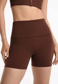 Brown high-waisted bike shorts made of stretchy fabric. Smooth texture with no visible patterns. Features a wide waistband for comfort.