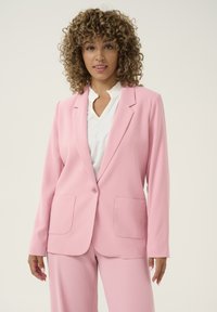 Růžový blazer s dlouhými rukávy, zapínání na jeden knoflík a dvěma předními kapsami, vyrobený z hladké látky. V kombinaci s odpovídajícími růžovými kalhotami.