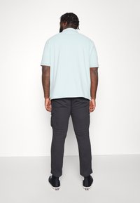Light blue polo shirt with short sleeves paired with dark cargo pants. The outfit features a loose fit and basic design.