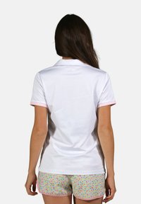 Polo blanc avec col et accents de manches roses, fabriqué en tissu lisse. Porté avec un short coloré à motif comprenant de petits dessins floraux.