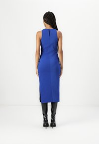 Rochie fără mâneci de un albastru regal, cu un design drept, având o fanta la spate și o închidere tip cheia. Asortată cu cizme lucioase negre până la genunchi.