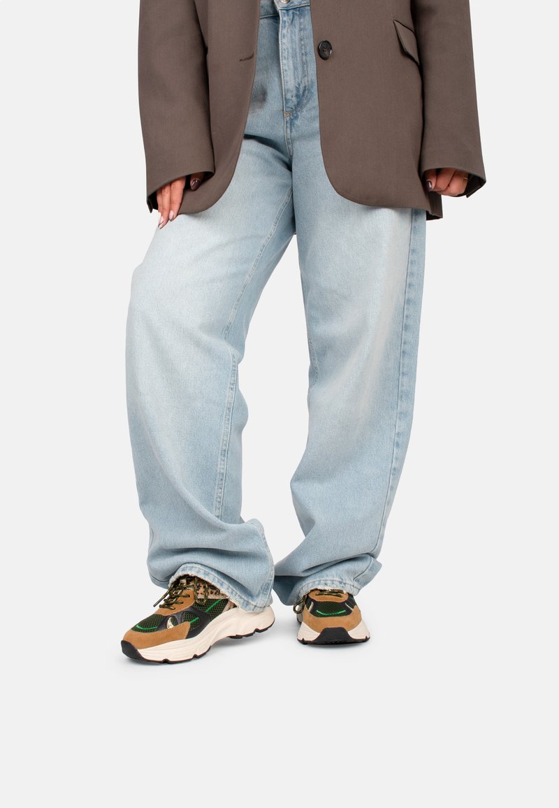 Jeans de pierna ancha de color azul claro combinados con un blazer oversized marrón. Presenta zapatillas gruesas con una mezcla de acentos verdes y marrones.