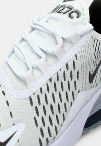 Gros plan d'une chaussure Nike Air Max 270 blanche avec des accents noirs, tissu en mesh, lacets et coussin d'air visible dans la semelle.