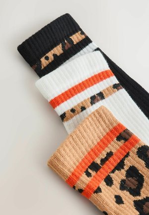 Schwarz-weiße und beige Socken mit Leopardenmuster, ausgestattet mit gerippten Bündchen und auffälligen orangen Streifen zur Kontrastierung. Weicher, strukturierter Stoff.