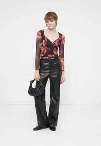 Pantaloni cu croi larg din piele neagră, asociați cu un top lung cu mâneci din material transparent, cu flori închise la culoare. Modelul ține o poșetă neagră. Textură netedă, design modern.