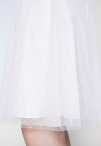 Witte tule rok met een gelaagd ontwerp, voorzien van een stippenpatroon en een iets rafelige zoom, die een lichte en luchtige textuur laat zien.