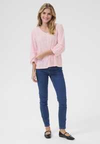 Top corto rosa brillante con maniche corte, scollatura a V e dettagli in pizzo. Abbinato a jeans aderenti blu e ballerine nere. Morbido tessuto.