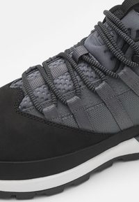 Gray athletic shoe featuring a mix of textured fabric and smooth suede, with a flexible sole, woven laces, and padded collar for support.