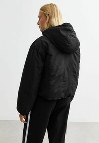 Chaqueta puffer corta negra con capucha, que presenta una textura suave, puños elásticos y un diseño minimalista. Adecuada para uso casual.
