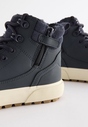 Stivali impermeabili grigio scuro con rivestimento in pelliccia sintetica, colletto alto, chiusura con zip e suola in gomma texturizzata per una migliore trazione.