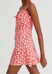 Rotes ärmelloses Kleid mit weißem Blumenmuster, strukturierten Trägern und ausgestelltem Saum, das ein Bindedetail am Ausschnitt aufweist.