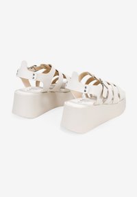 Sandalias de plataforma blancas con múltiples correas entrecruzadas, una textura suave y un tacón rectangular con acentos en plateado.