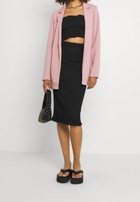 Czarny krótki top i spódnica z detalami falbanek, zestawione z jasnoróżową marynarką. Dodatki to czarna pleciona torebka i sandały na platformie.